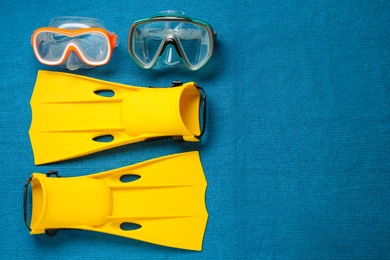 Photo of Pair of yellow flippers and masks on blue fabric, flat lay. Space for text