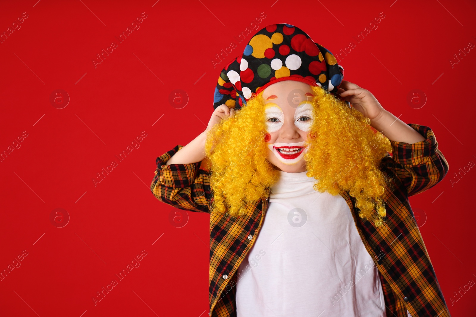 Photo of Funny little boy in clown costume on red background. April fool's day