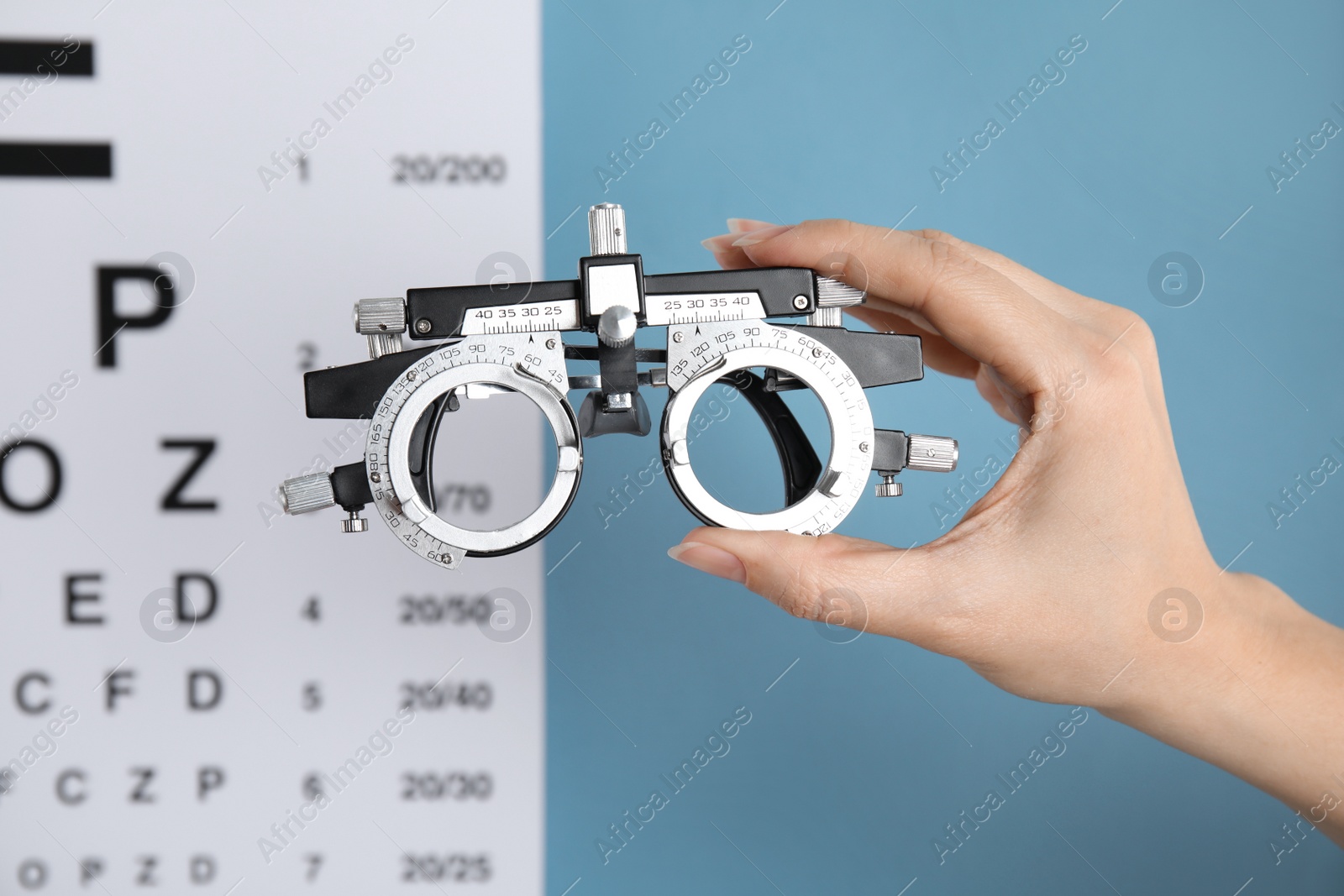 Photo of Woman holding trial frame against eye chart test on blue background, closeup. Ophthalmologist tool