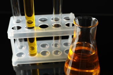 Laboratory glassware with different types of oil on black background, closeup