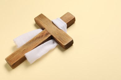 Photo of Wooden cross and white cloth on beige background, space for text. Easter attributes