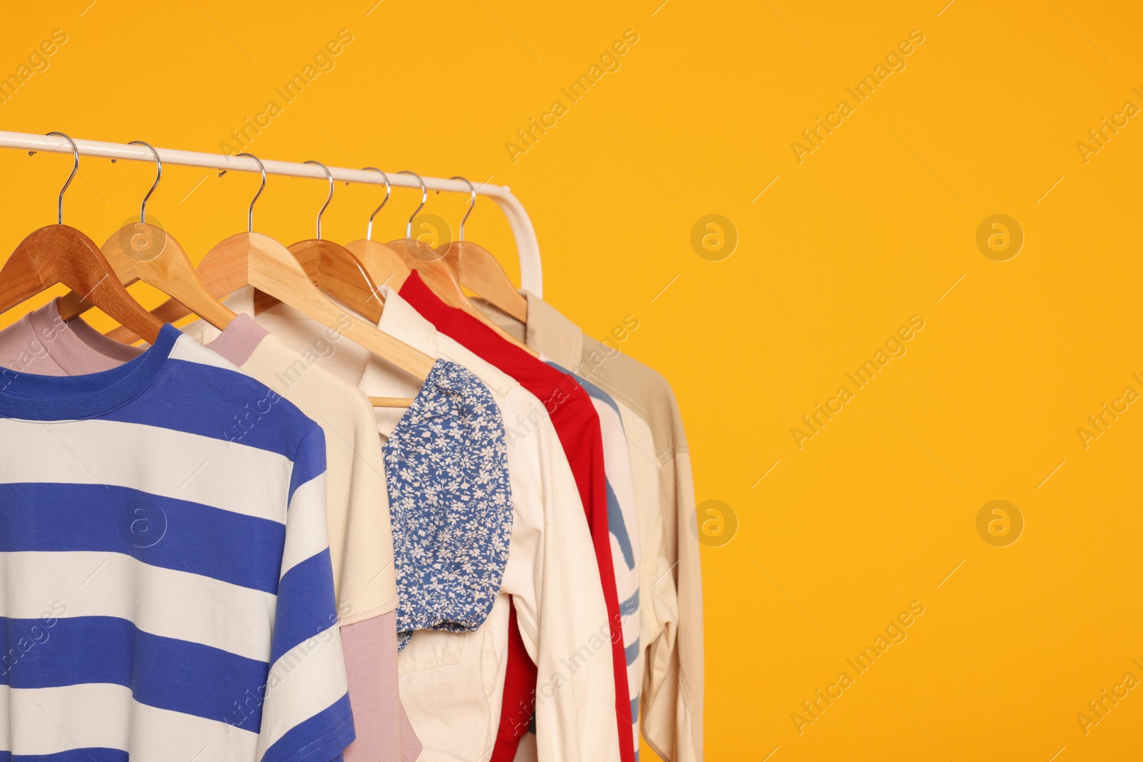 Photo of Rack with stylish women's clothes on wooden hangers against orange background, space for text