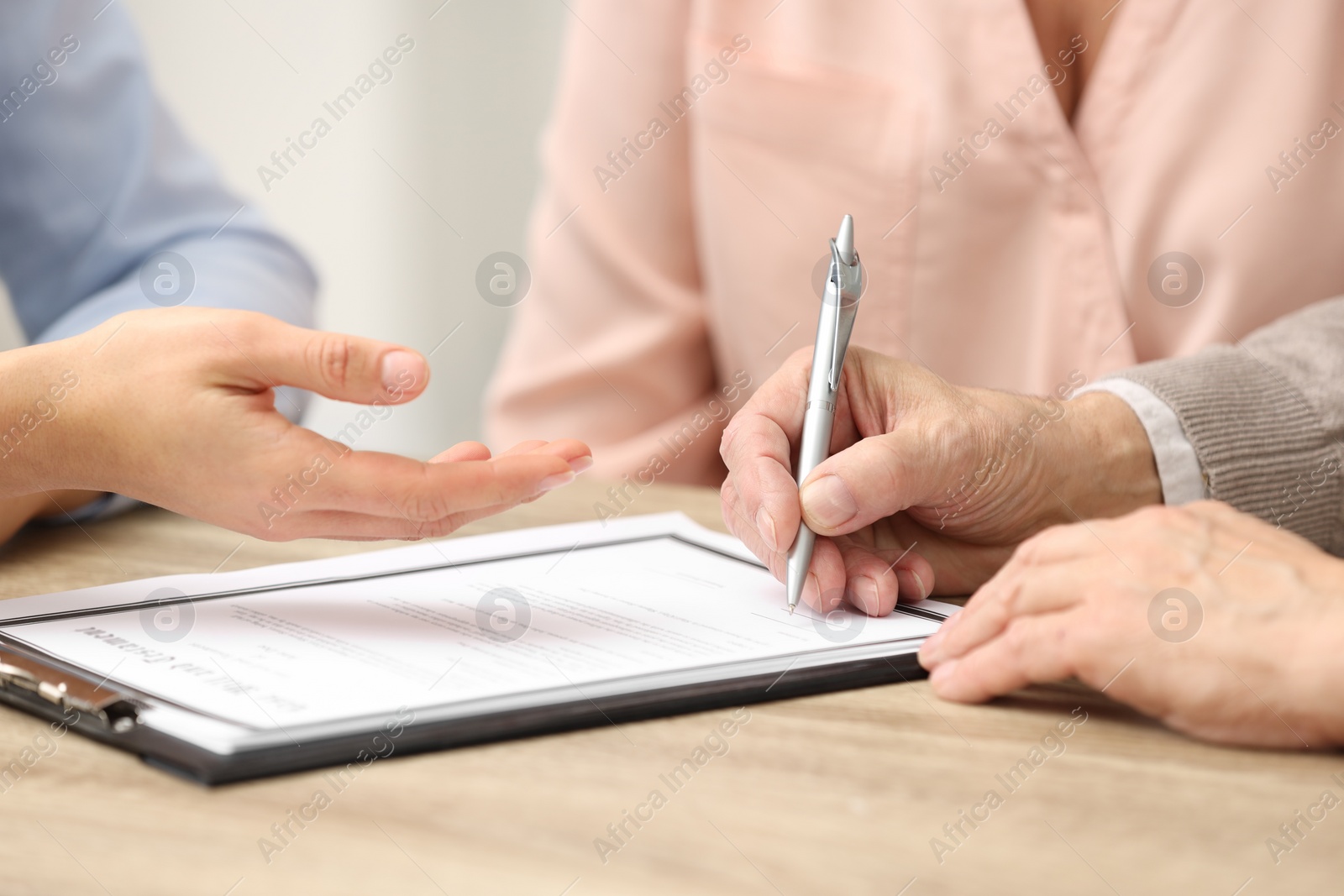 Photo of Notary showing senior man where to sign Last Will and Testament at wooden table, closeup