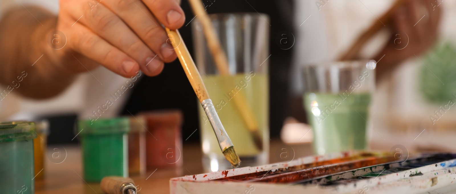 Image of Young man painting with brush in artist studio, closeup. Banner design