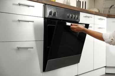 Photo of Woman opening modern electric oven in kitchen, closeup
