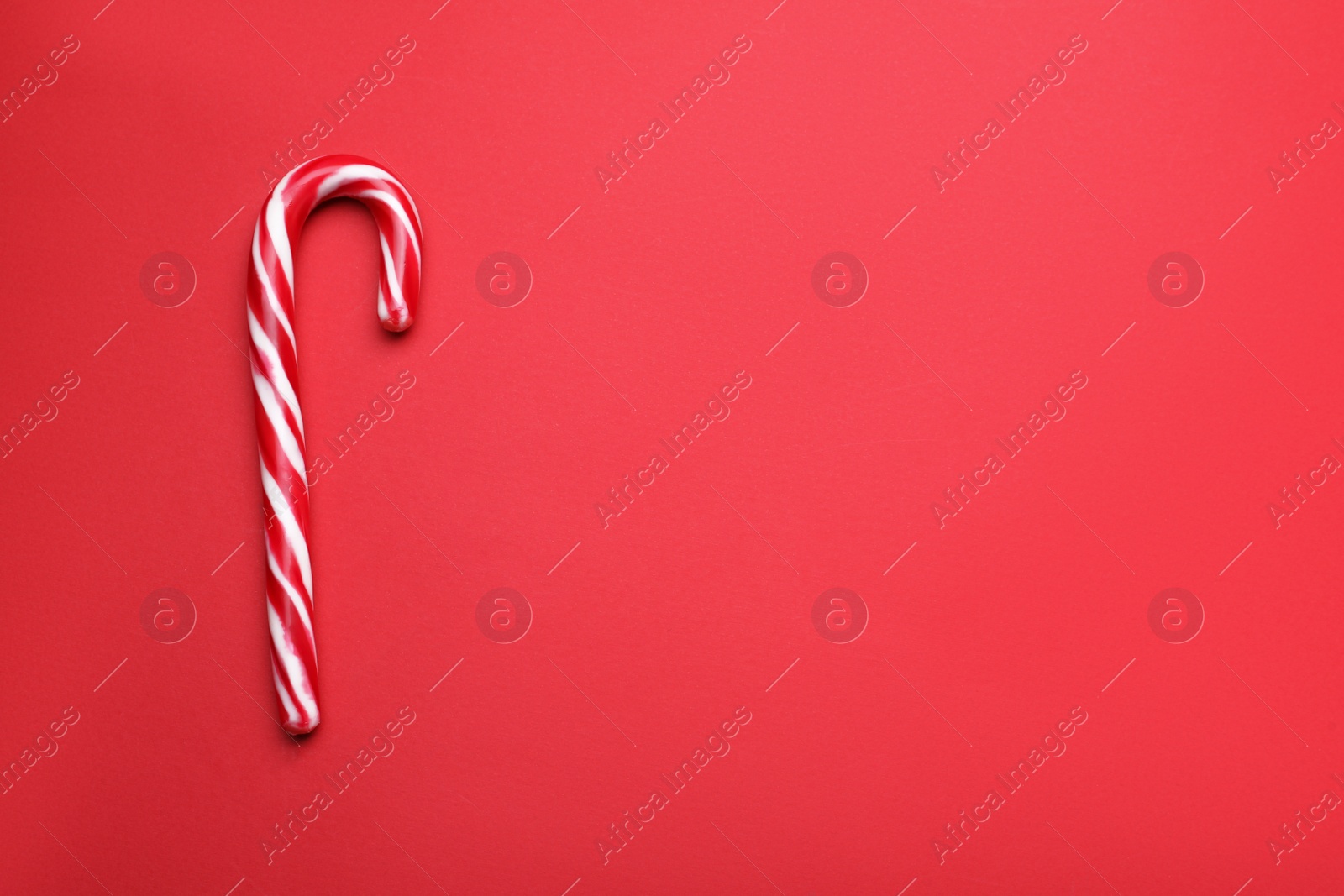 Photo of Sweet Christmas candy cane on red background, top view. Space for text