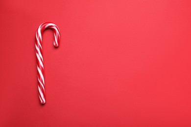 Photo of Sweet Christmas candy cane on red background, top view. Space for text