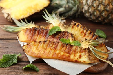 Tasty grilled pineapple pieces and mint leaves on wooden table, closeup