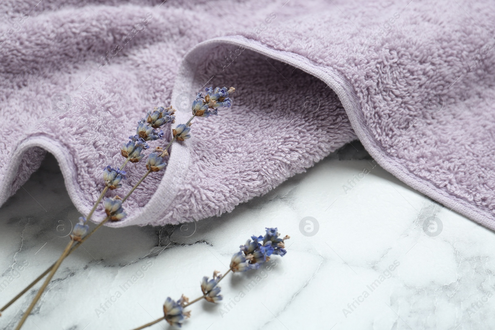 Photo of Violet terry towel and dry flowers on white marble table, closeup