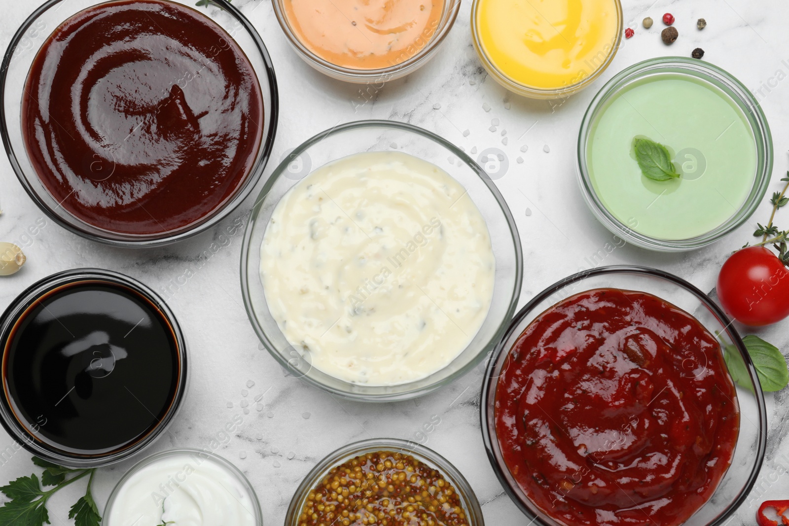 Photo of Many different sauces and herbs on white marble table