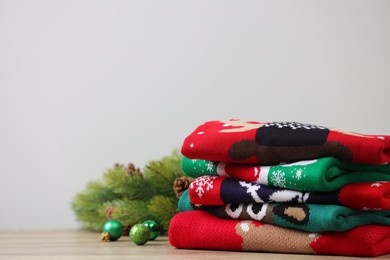 Photo of Stack of different Christmas sweaters, fir tree branch and baubles on table. Space for text