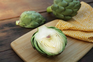 Photo of Whole and cut fresh raw artichokes on wooden table, closeup