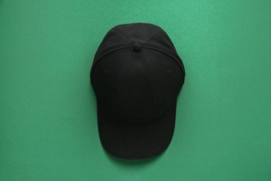 Photo of Stylish black baseball cap on green background, top view