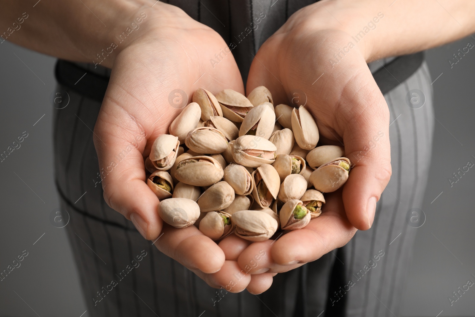 Photo of Woman holding organic pistachio nuts on grey background, closeup