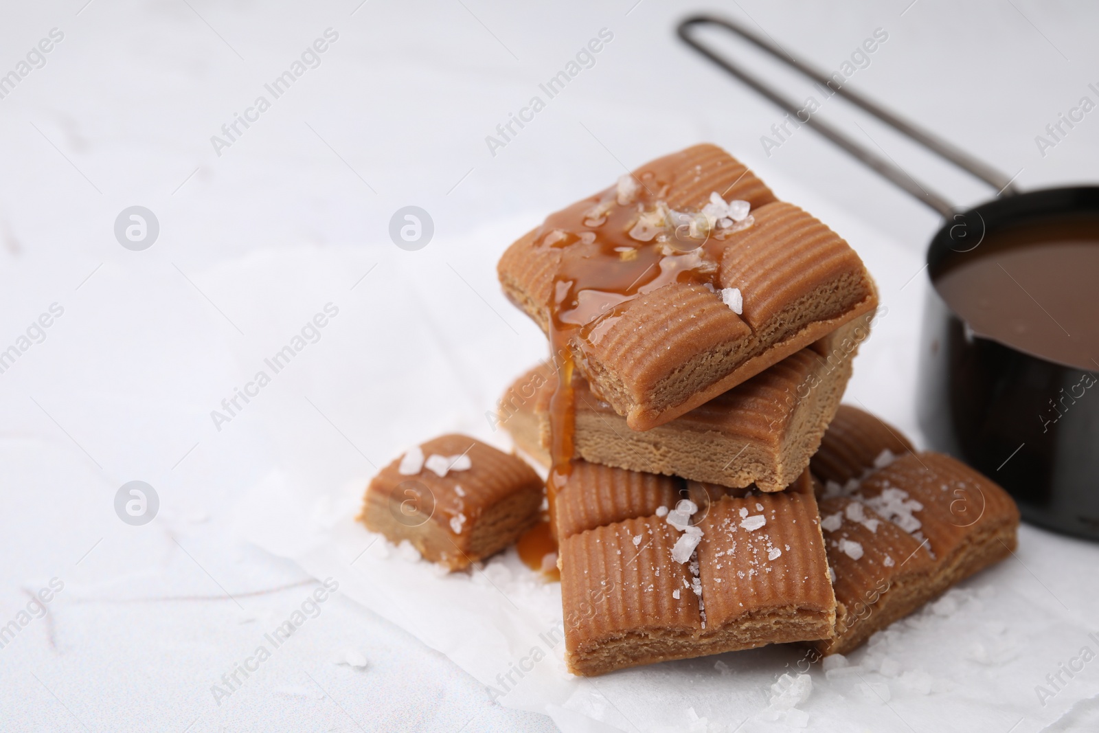 Photo of Yummy caramel candies, sauce and sea salt on white table, closeup. Space for text