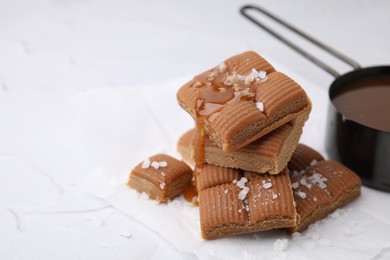 Yummy caramel candies, sauce and sea salt on white table, closeup. Space for text