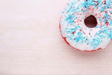 Photo of Glazed donut decorated with sprinkles on white wooden table, top view. Space for text. Tasty confectionery