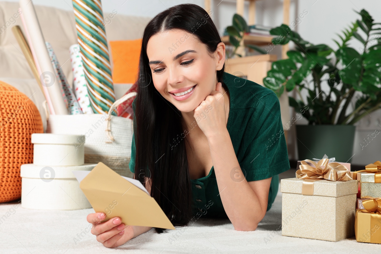 Photo of Happy woman reading greeting card on floor in living room