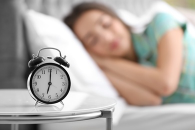 Photo of Alarm clock on table and woman in bedroom. Sleeping time