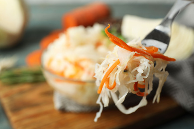 Fork with fermented cabbage on blurred background, closeup