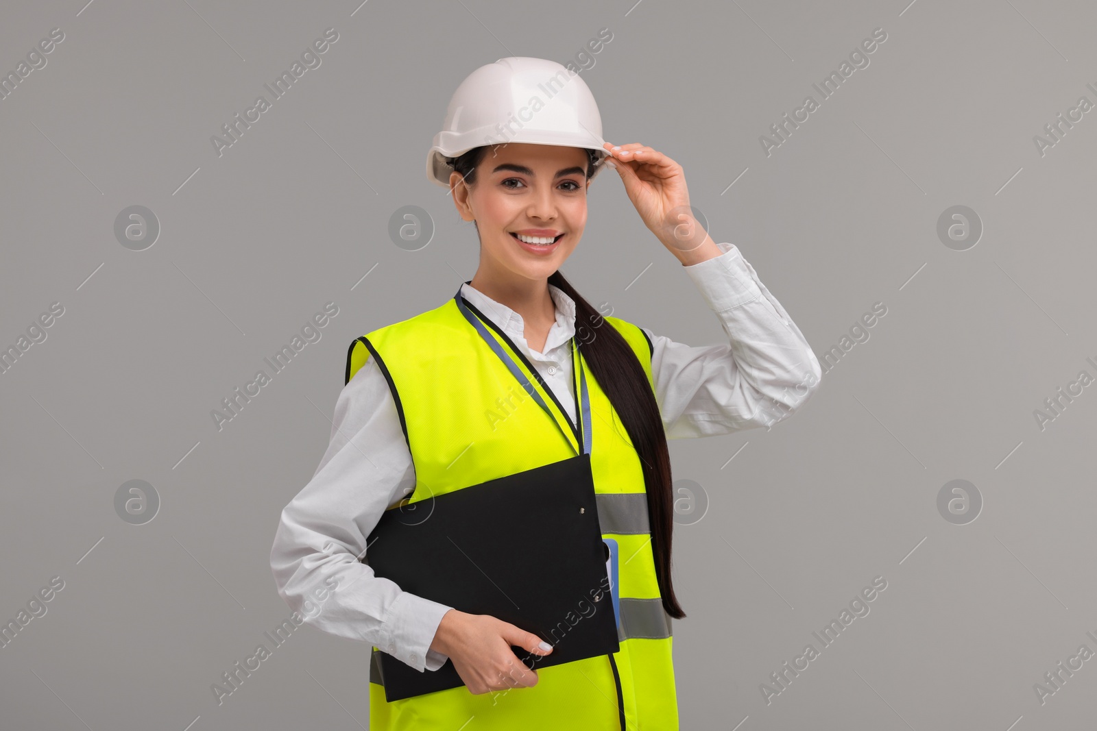 Photo of Engineer in hard hat holding clipboard on grey background