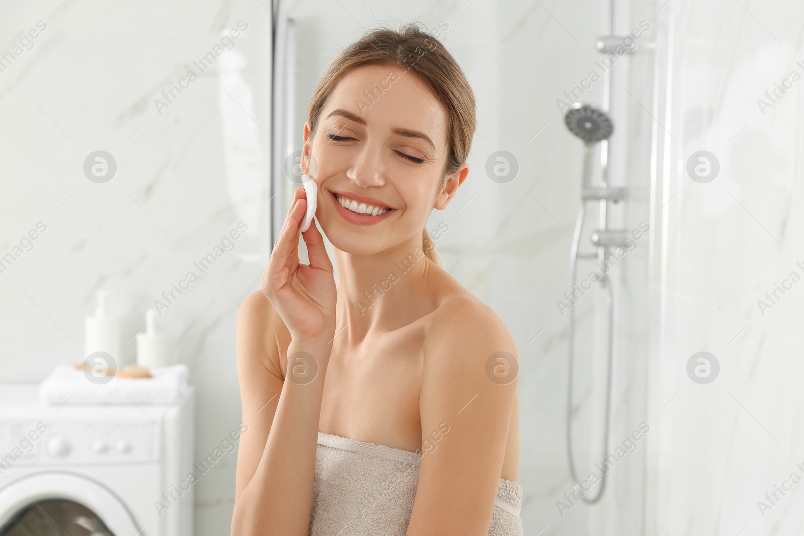 Photo of Young woman with cotton pad cleaning her face in bathroom