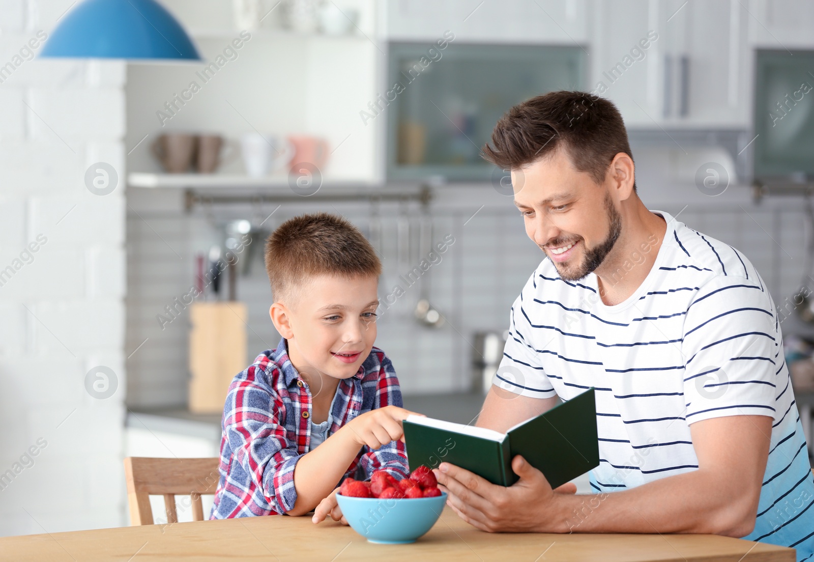 Photo of Dad and son reading interesting book in kitchen