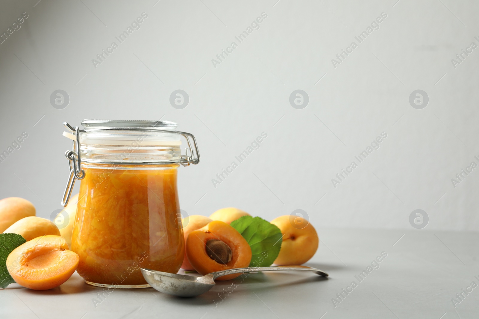 Photo of Jar of apricot jam and fresh fruits on light table. Space for text