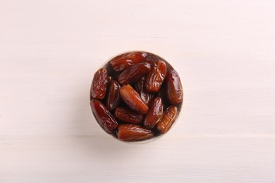 Photo of Sweet dried dates in bowl on white wooden background, top view