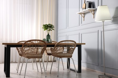 Photo of Rattan chairs, table, lamp and vase with green branches in stylish dining room