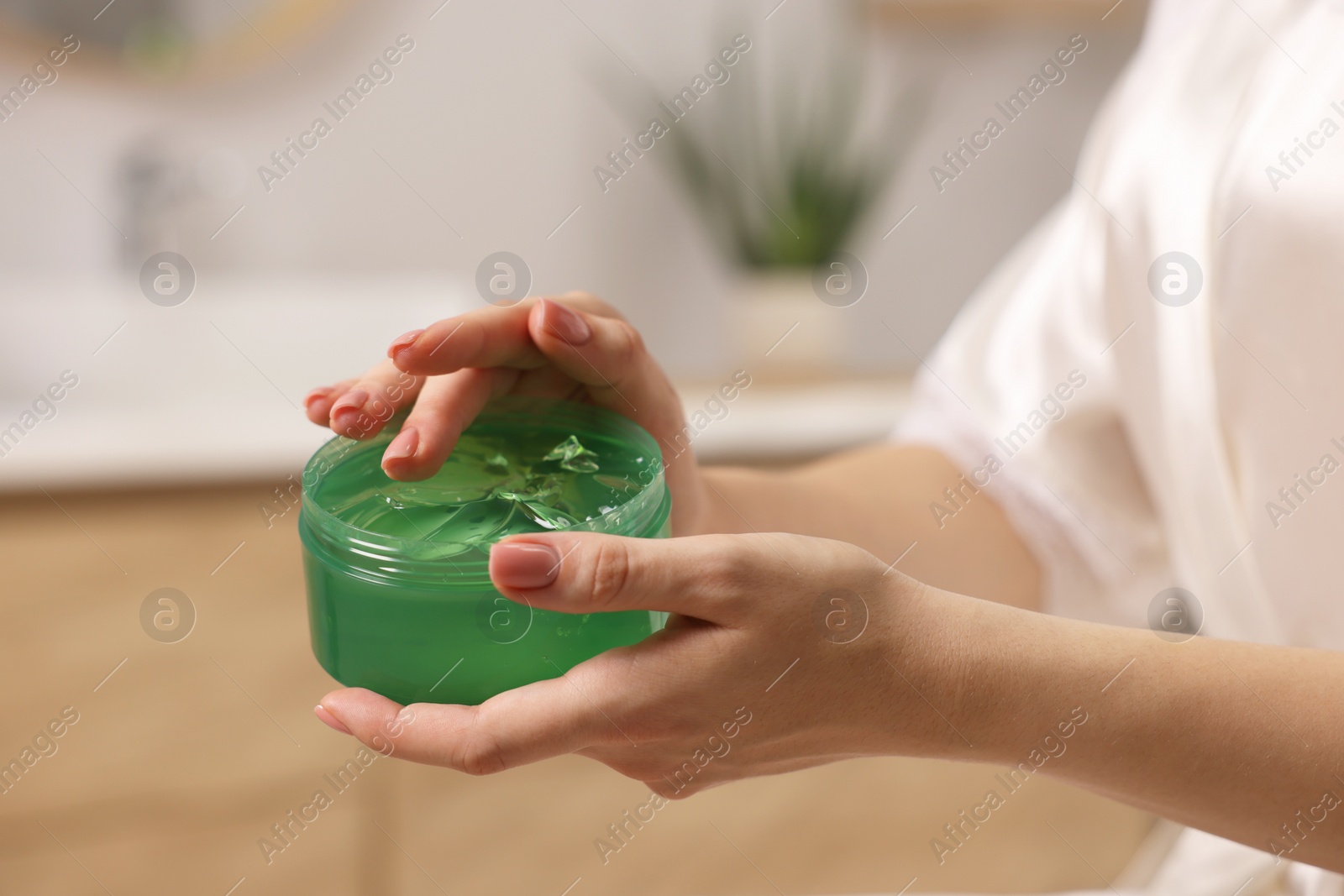 Photo of Young woman holding jar of aloe gel indoors, closeup