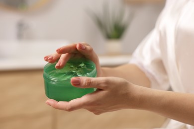 Young woman holding jar of aloe gel indoors, closeup