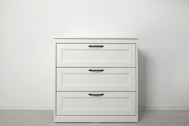 Photo of Modern wooden chest of drawers at light wall