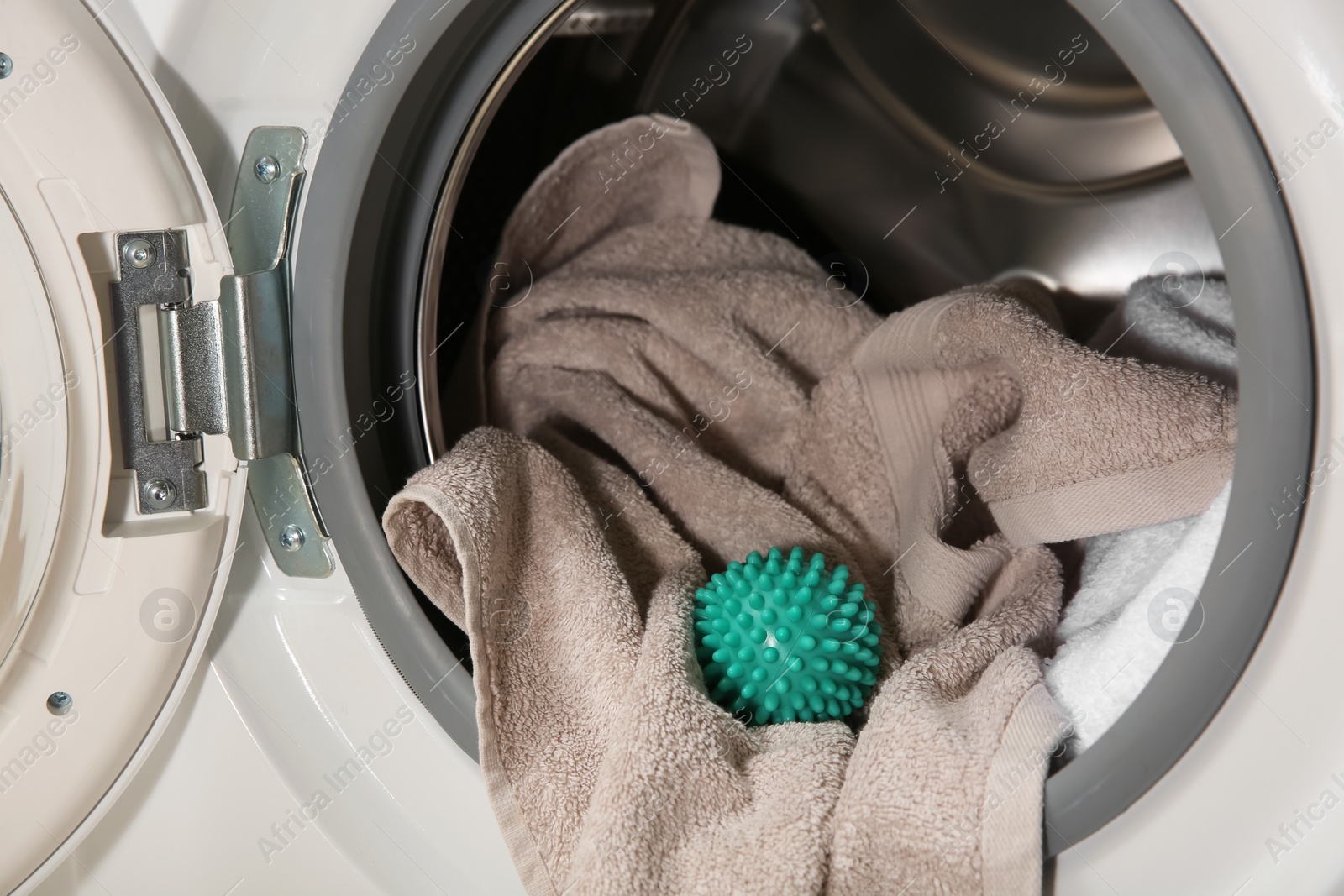 Photo of Green dryer ball and towels in washing machine drum, closeup