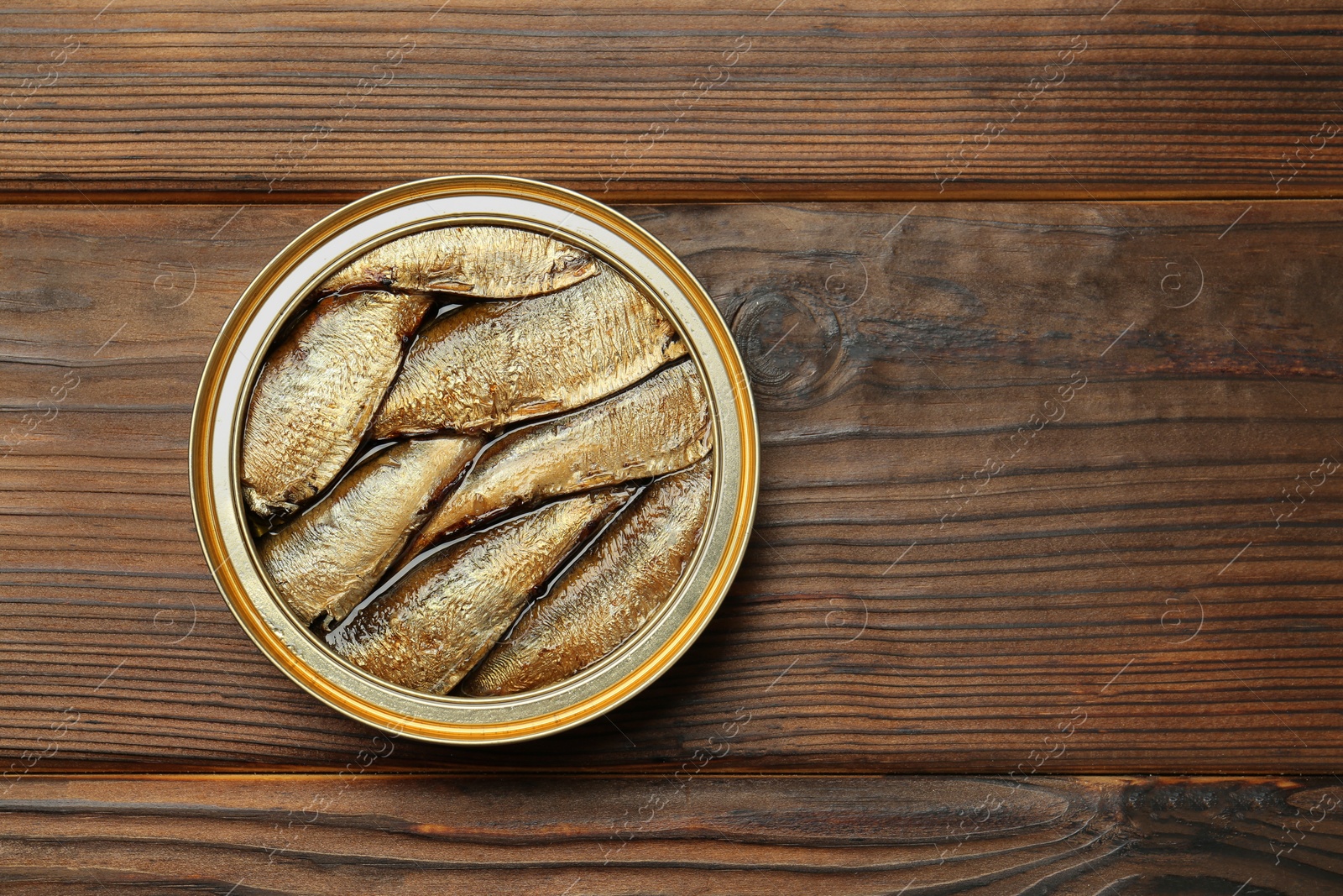 Photo of Open tin can of sprats on wooden table, top view. Space for text