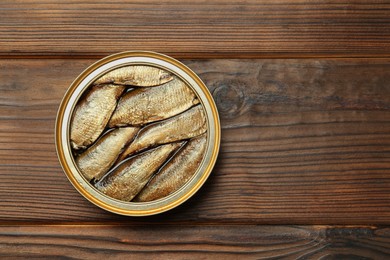 Open tin can of sprats on wooden table, top view. Space for text