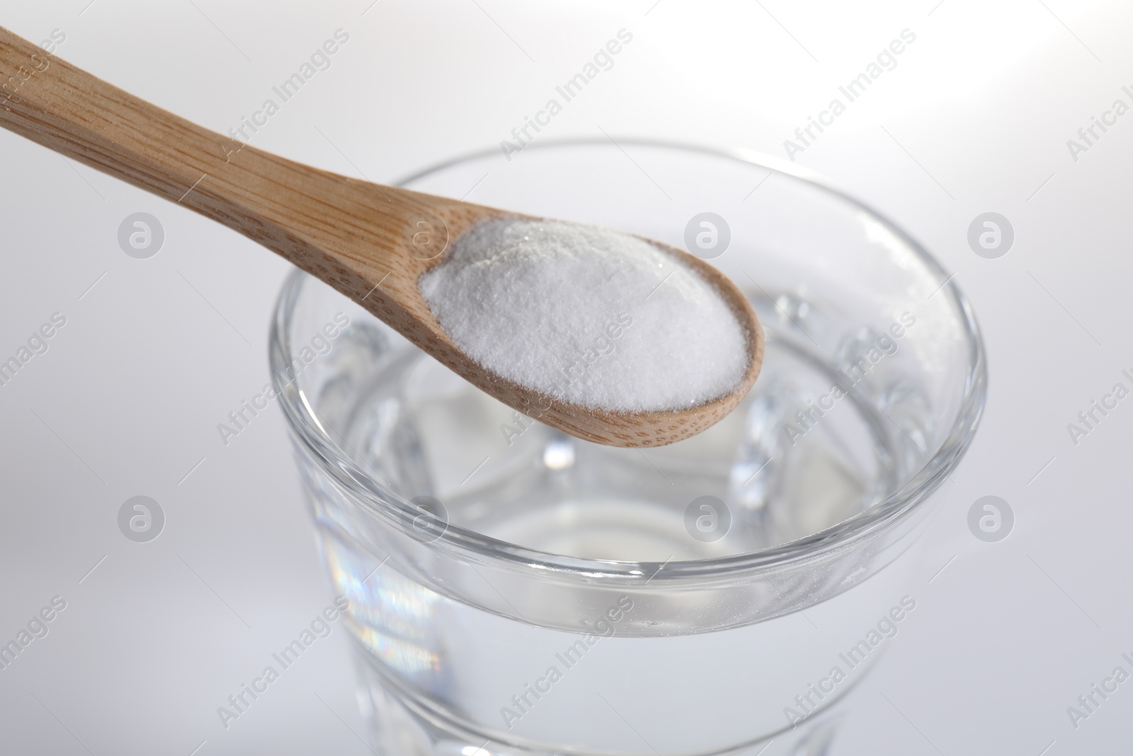 Photo of Spoon with baking soda over glass of water on white background, closeup