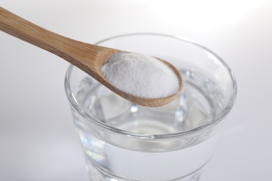 Photo of Spoon with baking soda over glass of water on white background, closeup