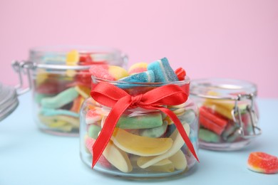 Glass jars with tasty colorful jelly candies on light blue table against pink background, closeup