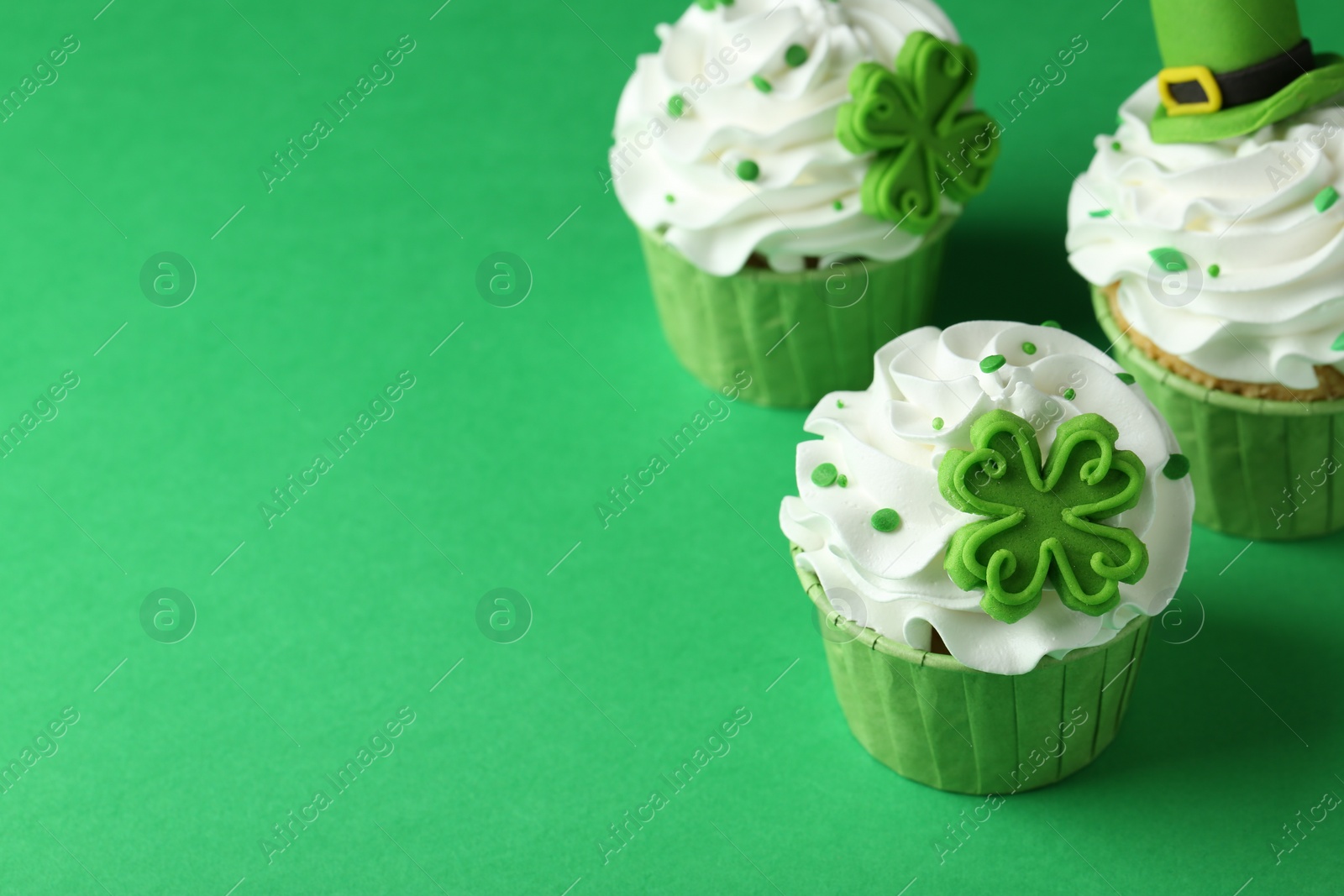 Photo of St. Patrick's day party. Tasty festively decorated cupcakes on green table, closeup. Space for text
