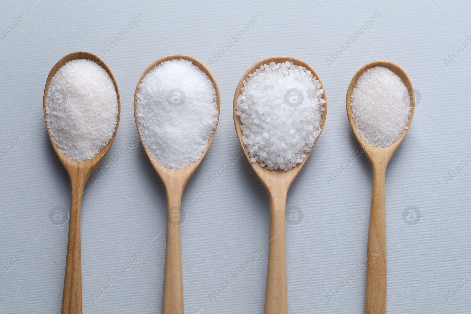 Photo of Organic white salt in spoons on light grey background, flat lay