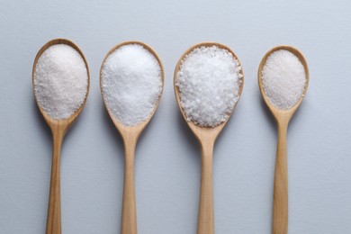 Photo of Organic white salt in spoons on light grey background, flat lay