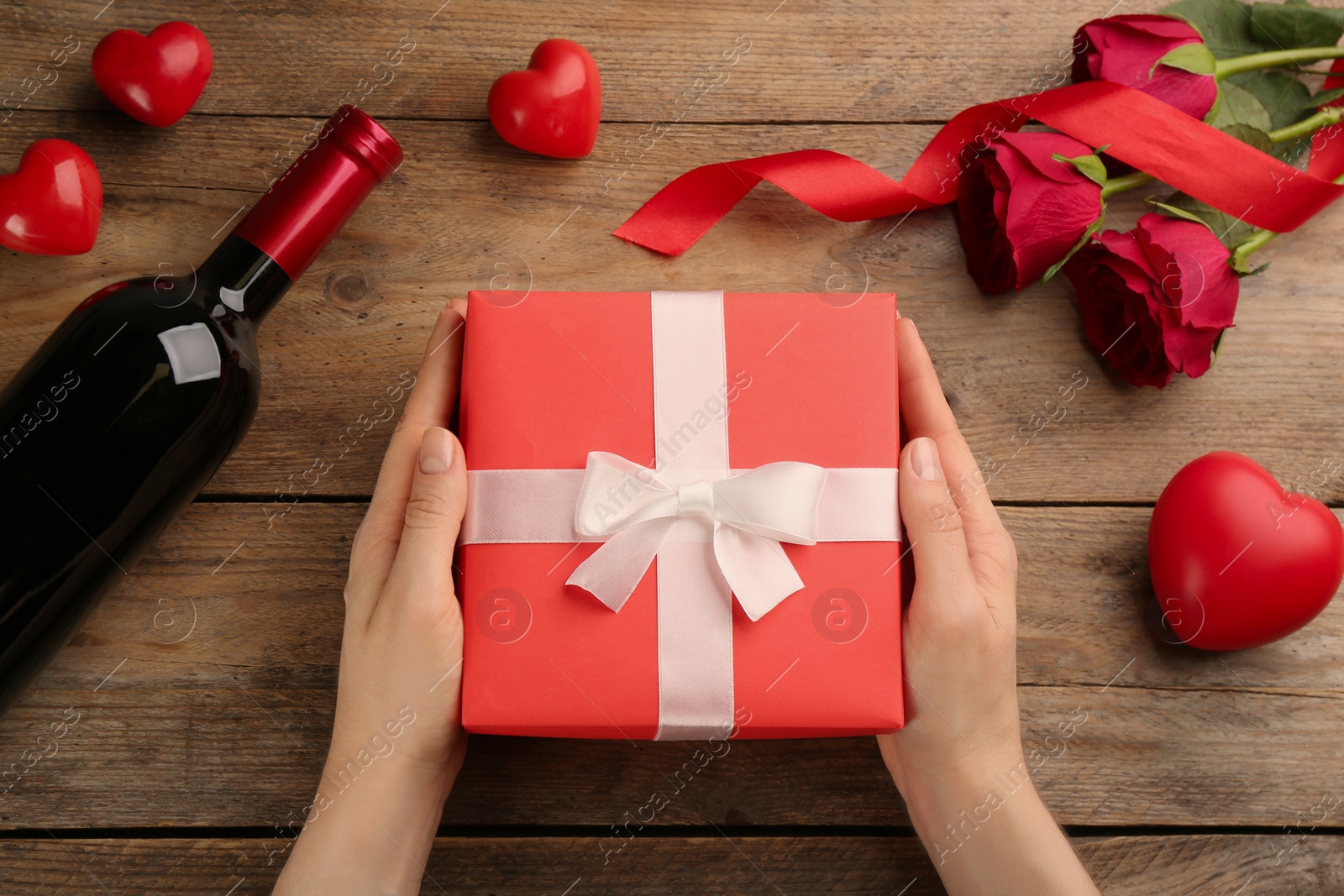 Photo of Woman holding beautiful gift box at wooden table, top view. Valentine's Day celebration