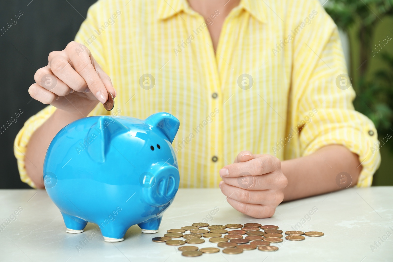Photo of Woman putting coin into piggy bank at light table, closeup