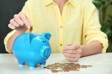 Woman putting coin into piggy bank at light table, closeup