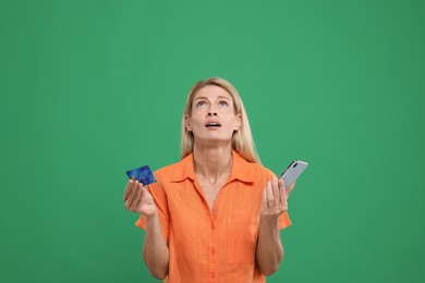 Photo of Emotional woman with credit card and smartphone on green background. Be careful - fraud