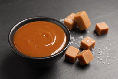 Photo of Yummy salted caramel in bowl and candies on black table