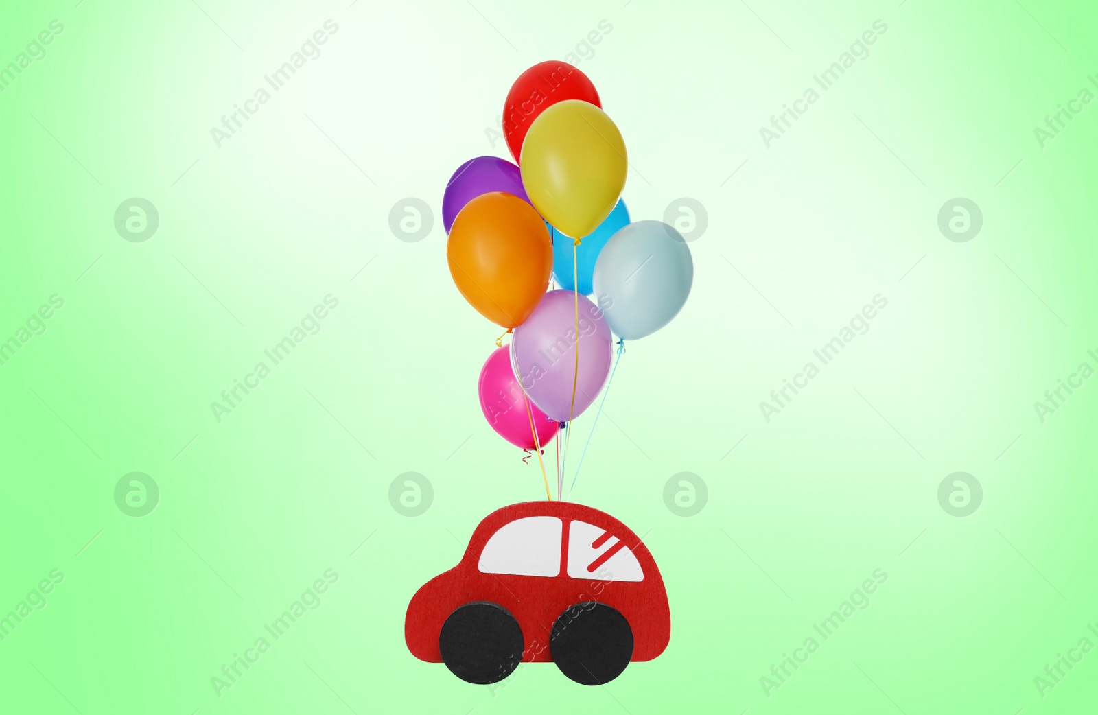 Image of Many balloons tied to toy car flying on light green background