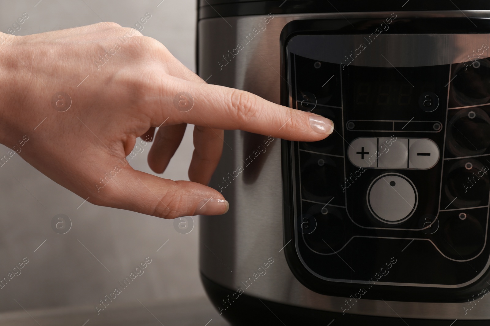 Photo of Woman turning on modern electric multi cooker on grey background, closeup