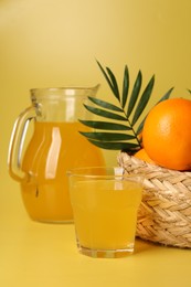 Photo of Fresh oranges in wicker basket and juice on yellow background